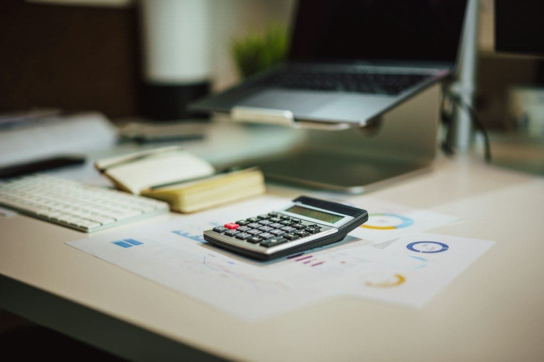 A calculator on a table next to a laptop, used to compare AI video clipper costs per hour
