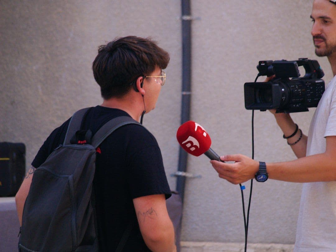 Two-person street interview: a camera operator films a young man answering into a handheld microphone, the kind of wide shot that is hard to convert from horizontal to vertical